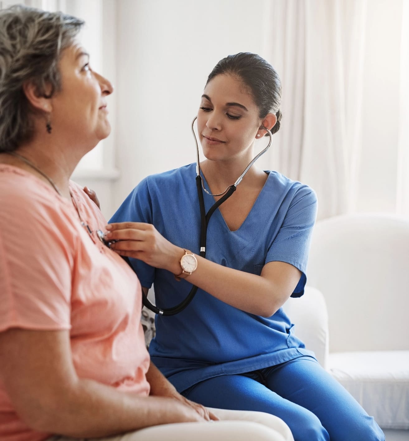 Nurse listening to elderly woman's heart with stethoscope.