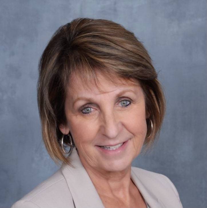 Professional headshot of a smiling woman with short brown hair wearing a blazer.