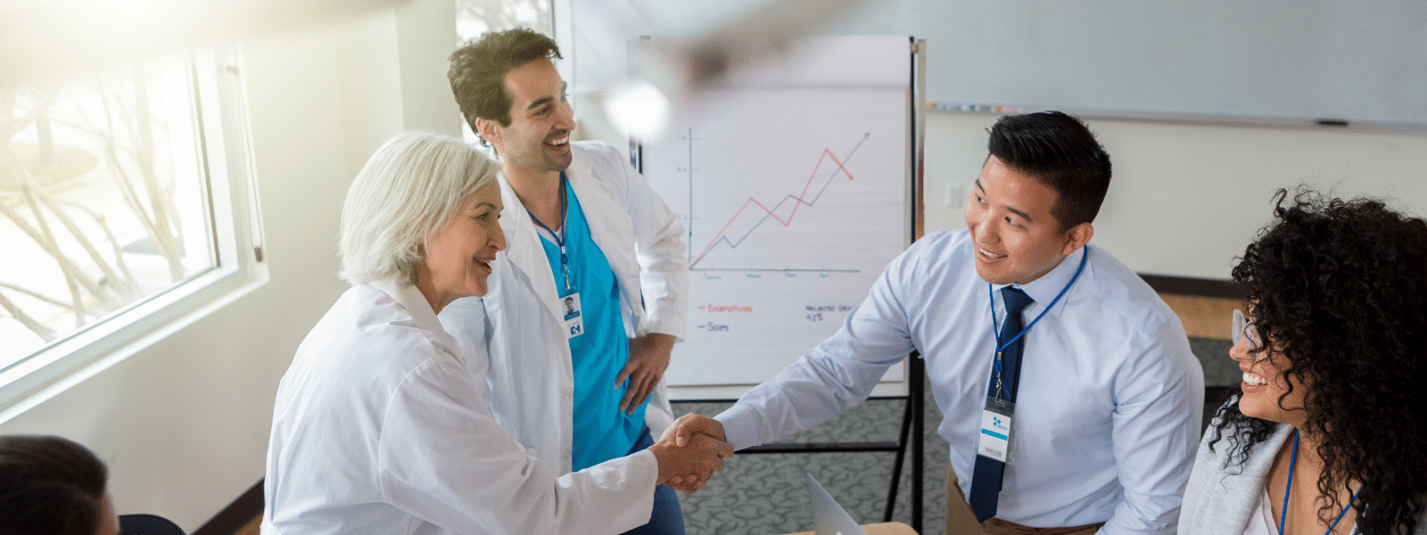 Doctors and business professional shake hands in a leadership coaching meeting.