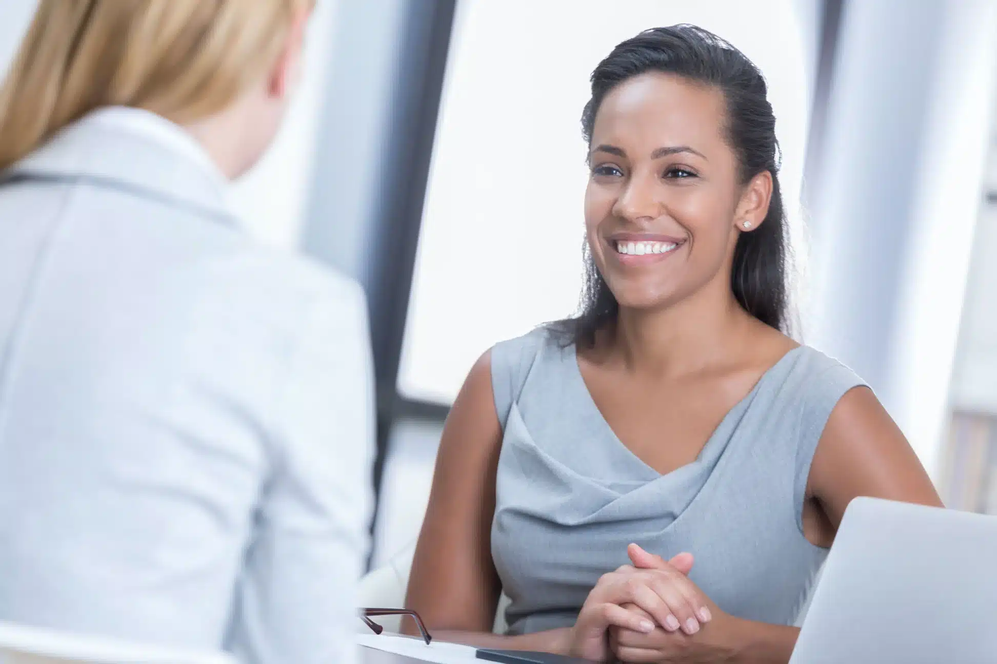 Smiling woman in a gray dress in a meeting, possibly discussing nurse leadership coaching.